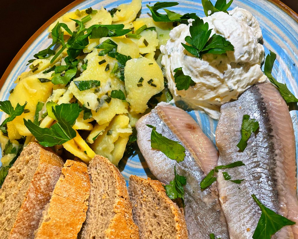 Matjesfilet auf Keramikteller mit Bratkartoffeln, Kräuterquark und dunklem Brot