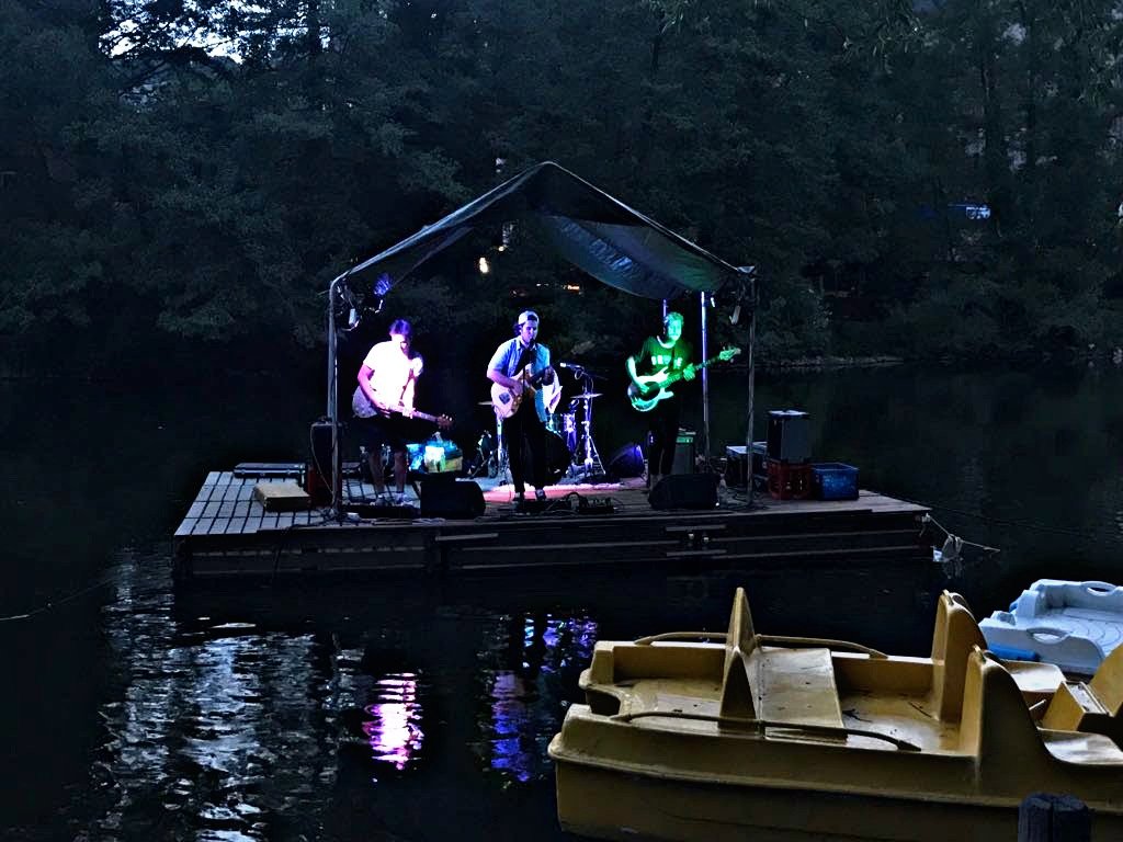 Band spielt auf der schwimmenden Bühne in der Abenddämmerung mit farbigen Scheinwerfern